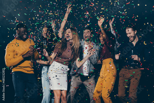Group of young happy people enjoying champagne and throwing confetti while dancing in night club