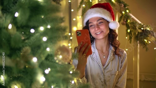Young caucasian woman in Christmas hat talks on the telephone. Girl wearing pajama set has a video conference. High quality 4k footage