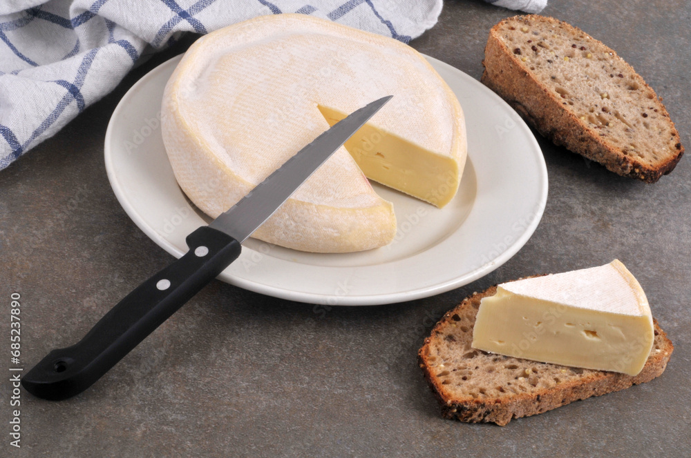 Reblochon dans une assiette avec un couteau et une tranche de pain aux graines avec un morceau de fromage. Reblochon dans une assiette avec un couteau et une tranche de pain aux graines avec un morceau de fromage.