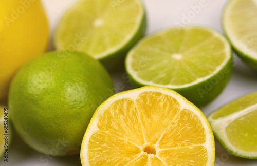 Many halves and slices of yellow lemon and green lime on light white table. Fresh fruits on kitchen top