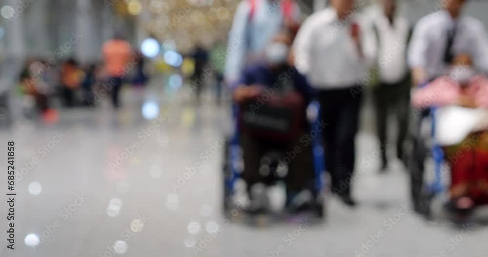 Blurred scene in modern airport terminal, featuring two elderly individuals in wheelchairs being assisted by airport personnel, with few accompanying people. Defocused picture for commercial use Blurred scene in modern airport terminal, featuring two elderly individuals in wheelchairs being assisted by airport personnel, with few accompanying people. Defocused picture for commercial use