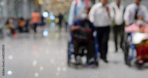 Blurred scene in modern airport terminal, featuring two elderly individuals in wheelchairs being assisted by airport personnel, with few accompanying people. Defocused picture for commercial use photo