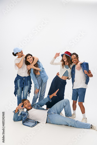 excited african american man lying down near happy interracial friends embracing on grey backdrop