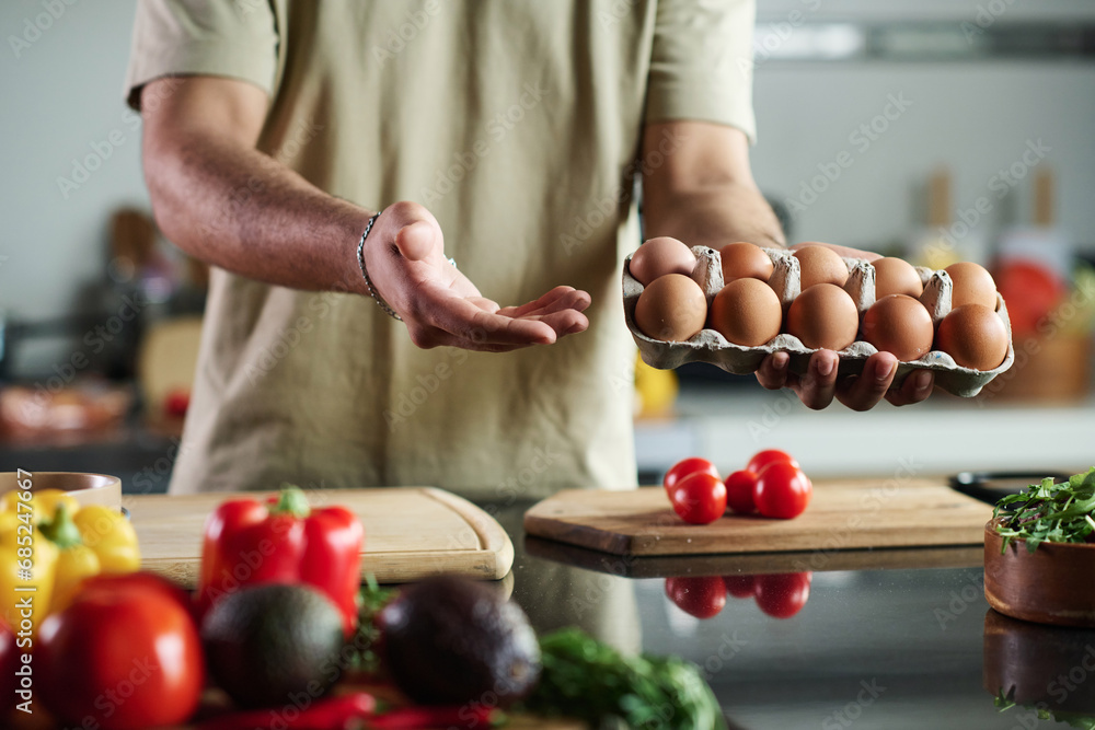 Close up of unrecognizable man holding carton of eggs above kitchen table Close up of unrecognizable man holding carton of eggs above kitchen table