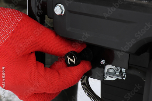A man in red gloves closes the carburetor choke before starting a cold gasoline generator engine photo