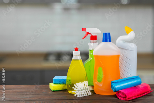 Cleaning products on a wooden table on a blurred kitchen background. Cleaning service concept. Household chemicals.Cleaning and detergents in plastic bottles, sponges and gloves.Mockup. Design. 