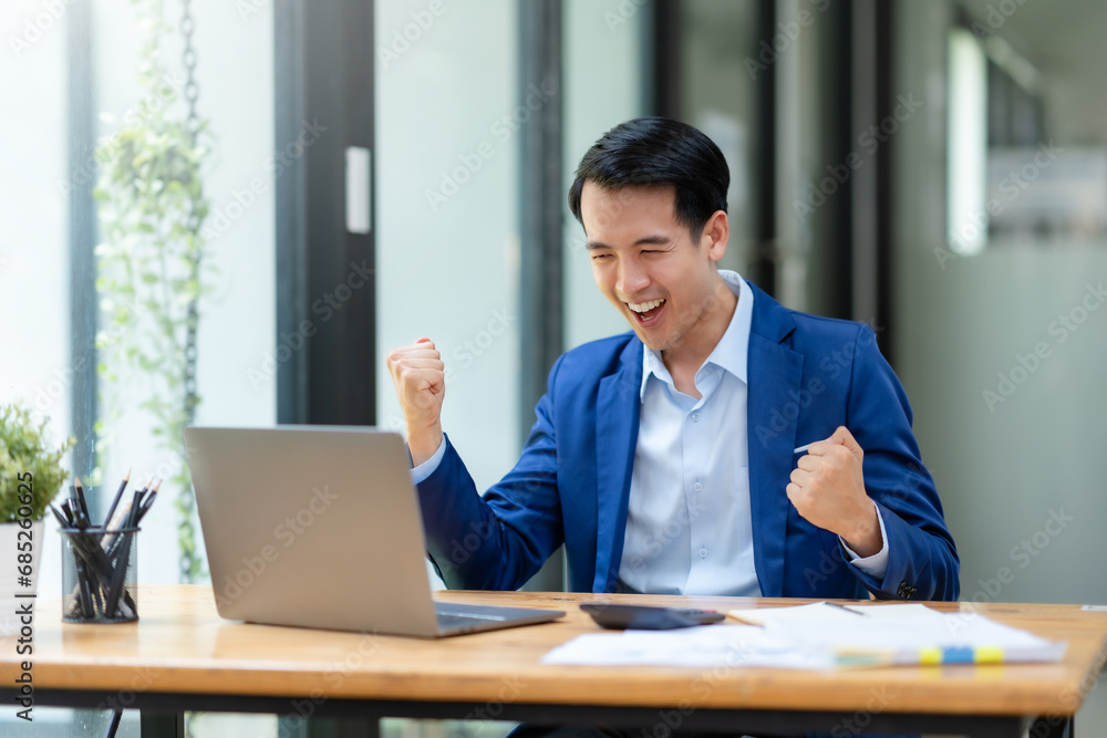 Excited cheerful asian businessman using laptop computer in the office, getting good news, feeling joy, laughing, making winner gesture, happy to win prize. Excited cheerful asian businessman using laptop computer in the office, getting good news, feeling joy, laughing, making winner gesture, happy to win prize.