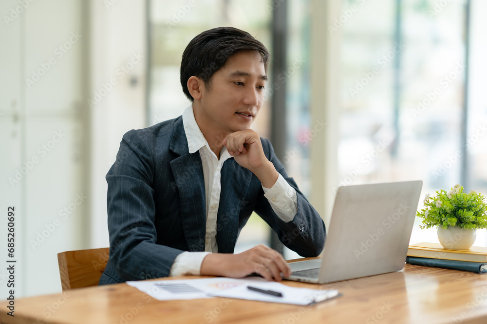 Smiling asian businessman using laptop computer at office. Confident Asia businessman sitting happily in the office. Smiling asian businessman using laptop computer at office. Confident Asia businessman sitting happily in the office.