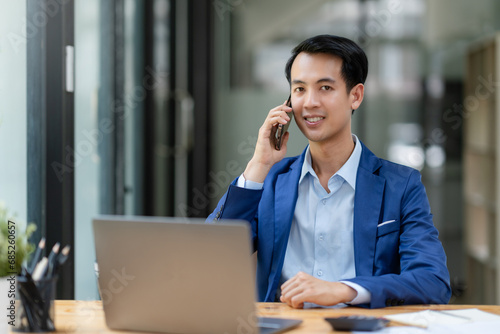 Asian businessman talking by smartphone in office. Smiling professional businessman manager talking on phone working communicating at work.