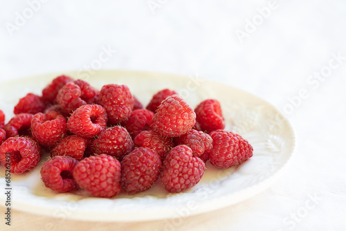 Fresh, ripe raspberries on a white plate, set against a white tablecloth. Perfect for a healthy snack or dessert.