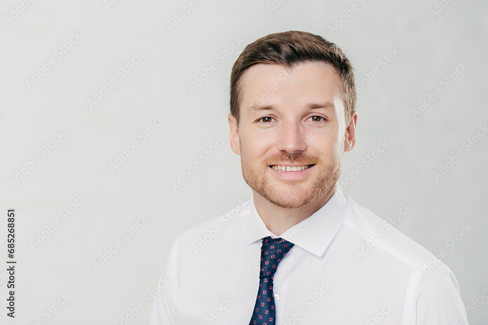 Confident young professional with a friendly smile, in white shirt and dotted tie, standing against a light background Confident young professional with a friendly smile, in white shirt and dotted tie, standing against a light background