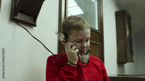 Portrait of european boy attentively listening to interlocutor in ancient telephone receiver. Alpha generation studies world history and familiarization with old communication technologies. photo