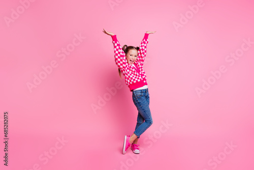 Portrait of overjoyed girl with fluttering ponytails wear print sweater denim pants raisng hands up isolated on pink color background photo