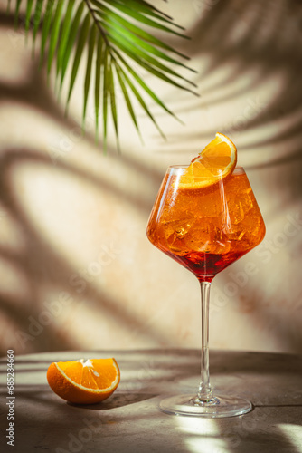 Glass of Aperol spritz cocktail with fresh oranges and palm leaves on beige background. natural light and shadows photo