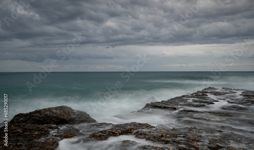 Stormy waves crashing on a rocky shore. Cloudy sky dangerous sea