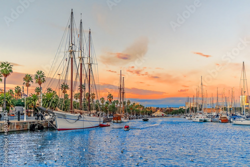 Evening seascape at Port Vell with a pirate galleon and many yachts against the backdrop of an orange-pink-blue sky in Barcelona, Spain. Beautiful cityscape of the Mediterranean coastline at sunset photo