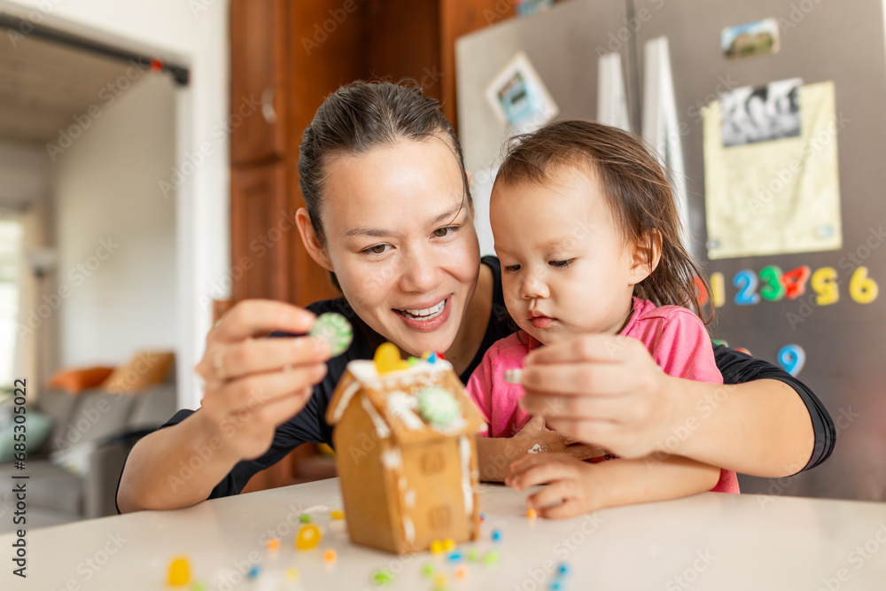 Fototapeta premium Mother and cute little girl decorating gingerbread house at home Happy family Christmas activity.