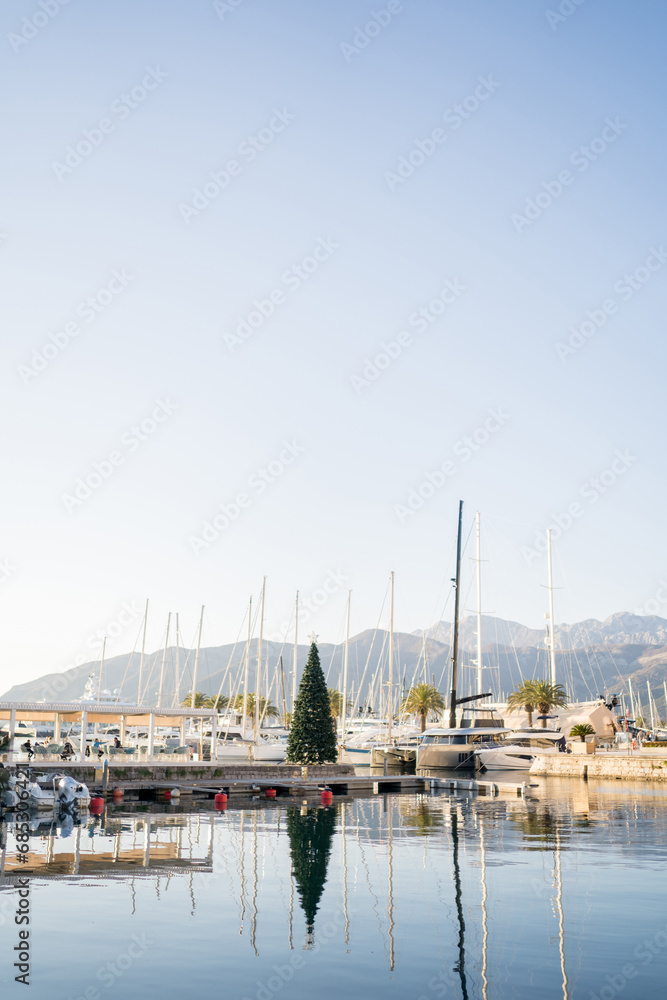 Christmas tree stands on the pier near moored sailing yachts against the backdrop of the mountains. Porto, Montenegro
