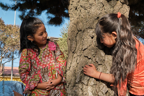 two orphaned latin girls playing with a tree in an outdoor park - friendship concept