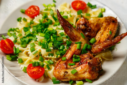 Farfalle pasta with grilled chicken wings garnished with cherry tomatoes and green onions. Close-up