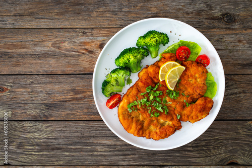 Crispy breaded fried chicken cutlet with boiled broccoli and fresh vegetables on wooden table
 photo