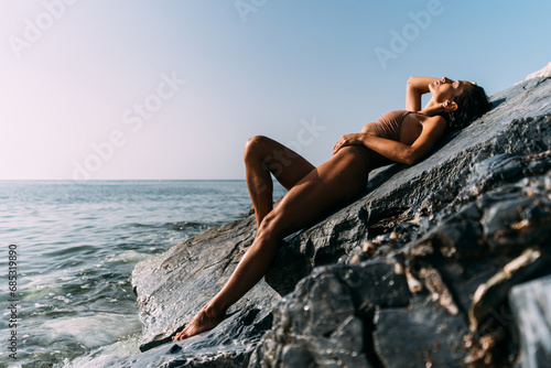 A beautiful young, sensual woman in a swimsuit is lying on the rocks by the sea.