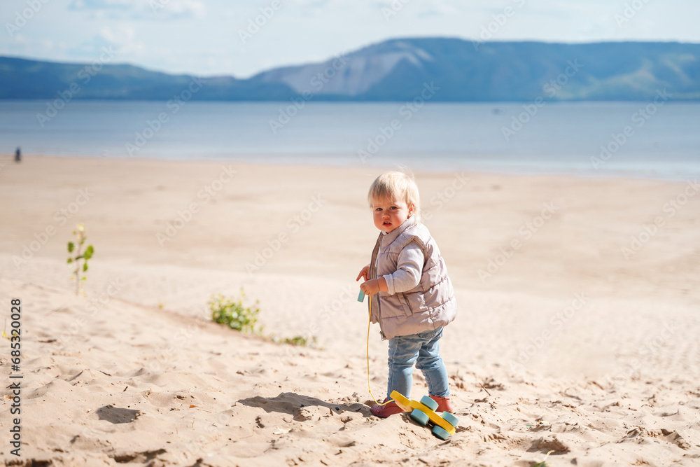 An adorable little toddler is walking along an empty cold beach with a duck toy, a beautiful landscape and a cute childhood concept, northern cold nature An adorable little toddler is walking along an empty cold beach with a duck toy, a beautiful landscape and a cute childhood concept, northern cold nature