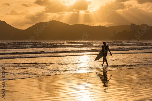 City of Santos, Brazil. Surfer entering the water. Golden hour sunset on Santos beach, Porchat Island at right.