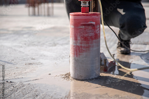 A worker drills a reinforced concrete floor using a drilling rig with a diamond bit.