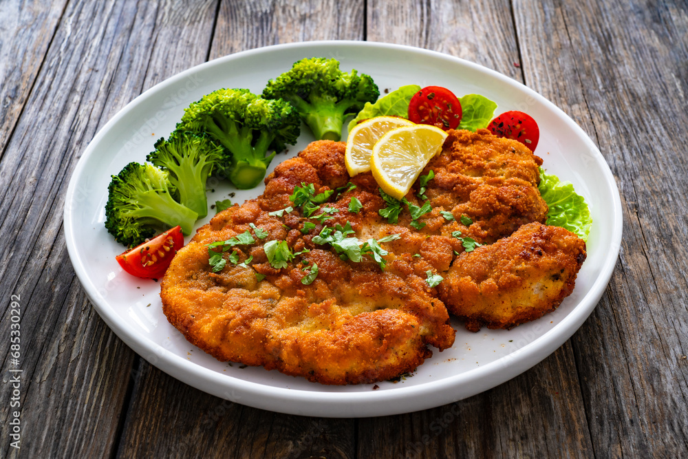 Crispy breaded fried chicken cutlet with boiled broccoli and fresh vegetables on wooden table
Crispy breaded fried chicken cutlet with boiled broccoli and fresh vegetables on wooden table
