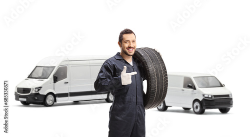 Auto mechanic in front of vans holding a tire and pointing © Ljupco Smokovski