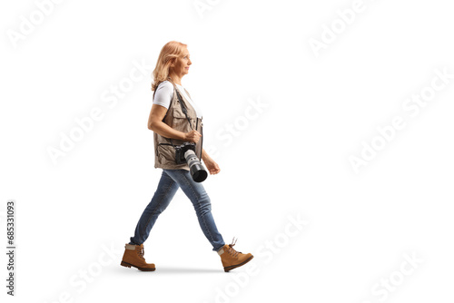 Full length profile shot of a female photographer walking with a camera on a shoulder strap
