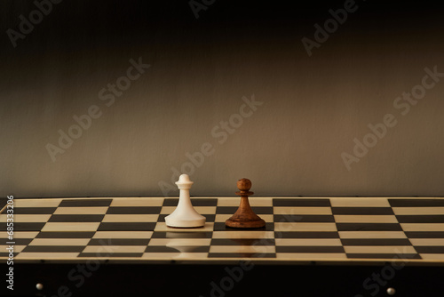 Two chess pawns  wooden and marble  stand facing each other on a chessboard. Confrontation of opposites  struggle between old and new  the initial level of battle