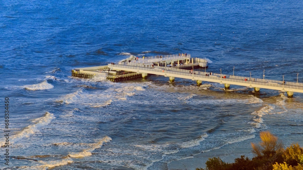 Obraz premium A bird's eye view of the Kołobrzeg pier. Photo taken by a drone showing the pier and the rough, blue Baltic Sea.