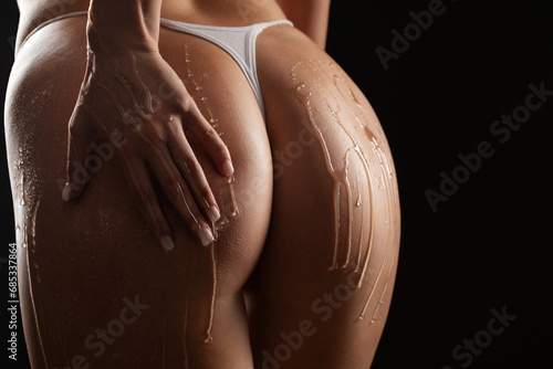 Beautiful sexy ass of young naked woman on black background. Drops of honey flow down on her buttocks photo