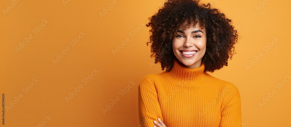 A young woman in an orange sweater poses with her curly hair for a photo in a studio. A young woman in an orange sweater poses with her curly hair for a photo in a studio.