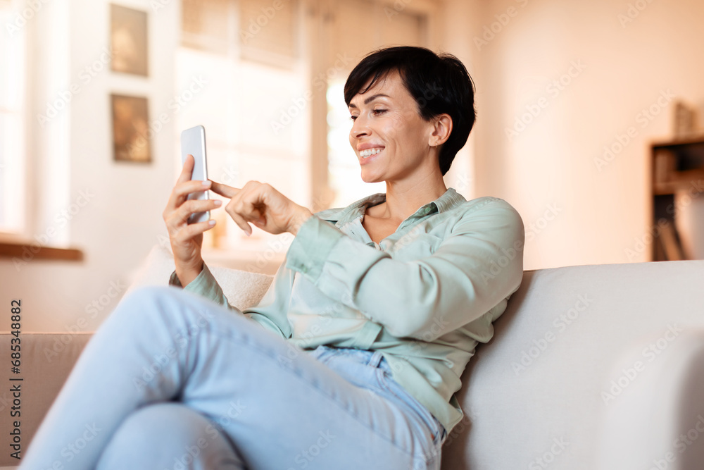 Middle aged lady browsing her smartphone in living room Middle aged lady browsing her smartphone in living room