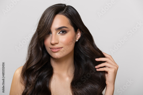 Beautiful young woman with wavy long hair flying to the side. Portrait on a gray background