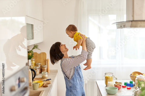 Mother lifting up her baby boy in the air in the kitchen photo