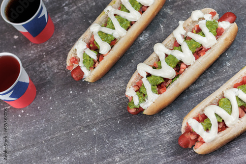 Completo Italiano Chileno: hot dog bun with vianesa, tomato, palta and mayo with poly paper cups chilean flag on chilean national holidays. on cement table. Typical Chilean food concept