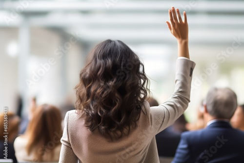 The rear view captures a casual businesswoman in a conference, energetically raising her arm to signify engagement and proactive participation.