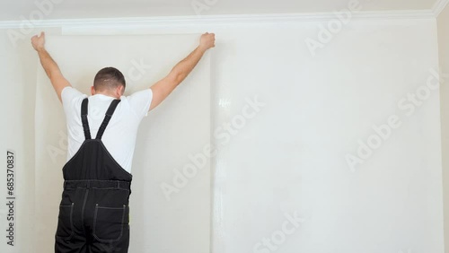 Men applying brand new modern wallpaper on his apartment walls. Home improvement theme.