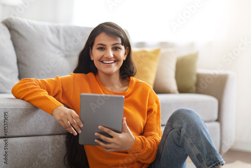Happy indian woman sitting on floor at home, using tablet