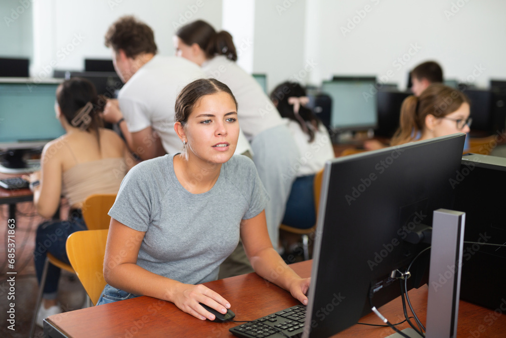 Fototapeta premium Surprised girl student sitting at her workplace and studying in college computer class