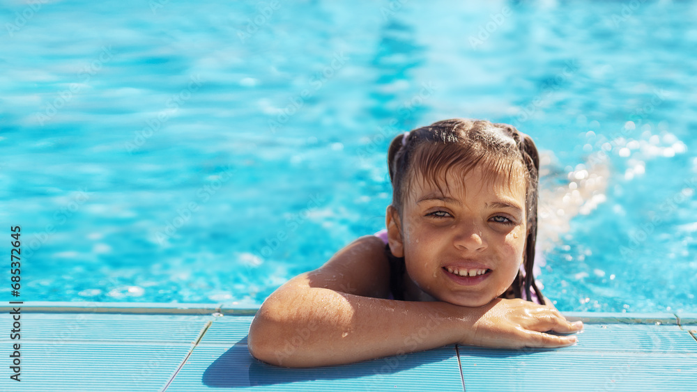 Portrait of happy smiling 7 years old girl in swimming pool on sunny day