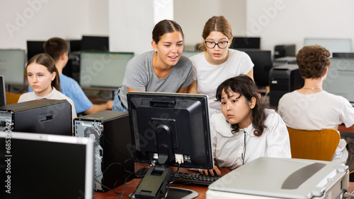 Serious teenagers helping to the focused female classmate while she is learning computer science in the class