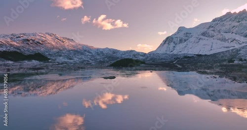 Aerial view from low flying drone of sea coast, snowy mountains in winter at sunrise. Lofoten islands, Norway. Top view of fjord, reflection, water, stones, snowy rocks, purple sky with clouds. Lake photo