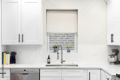 A white kitchen detail with an arabesque backsplash tile, a stainless steel faucet and sink, and a white marble countertop.
