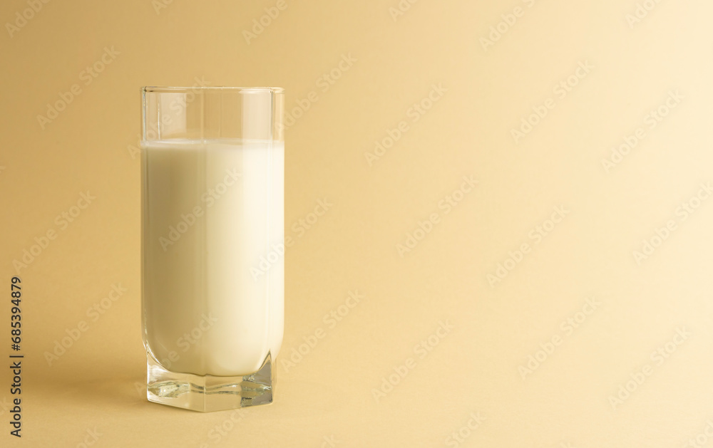 A glass of milk is isolated on a beige background. Close up of the dairy product. A glass of milk is isolated on a beige background. Close up of the dairy product.