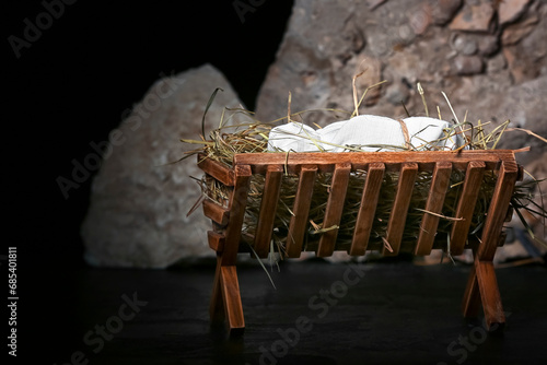 Manger with baby, hay and stones on dark background